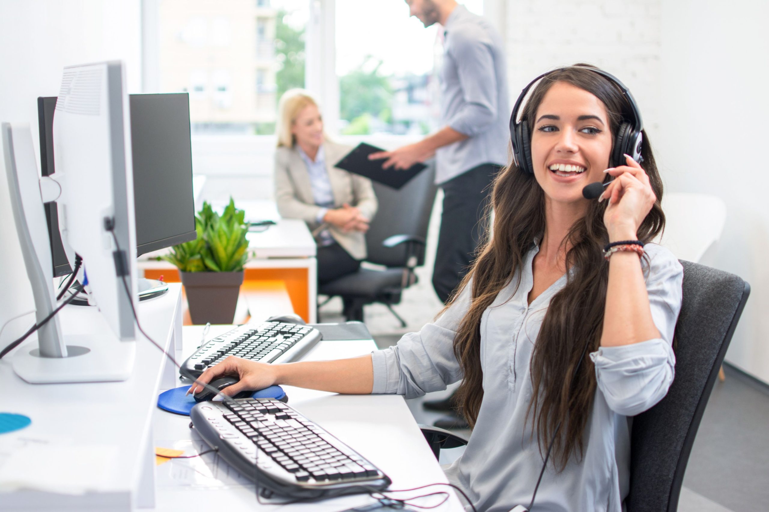 Young female office worker with headset on, smiling during a call