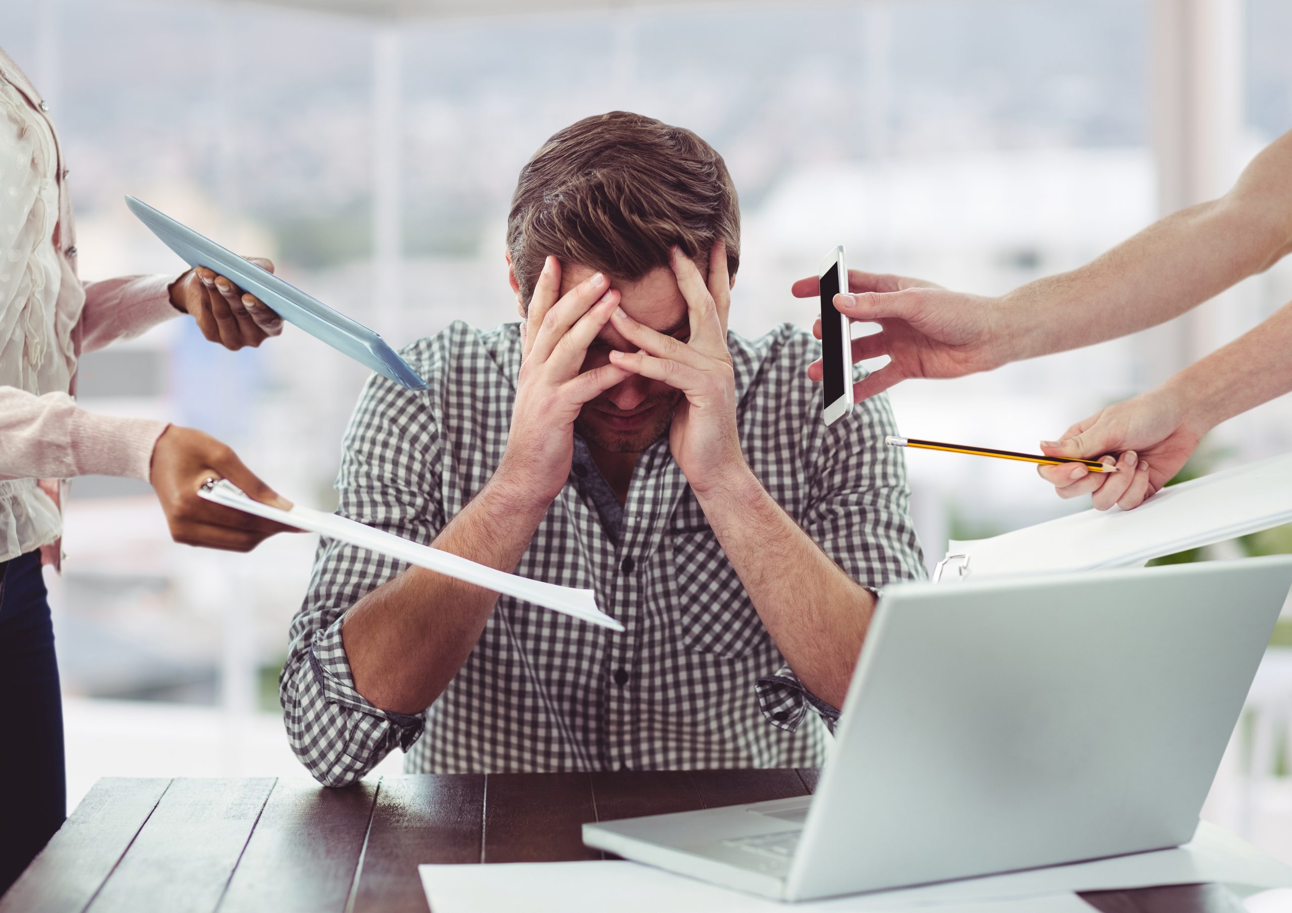 Stressed worker with devices in his face from other employees asking him to do work